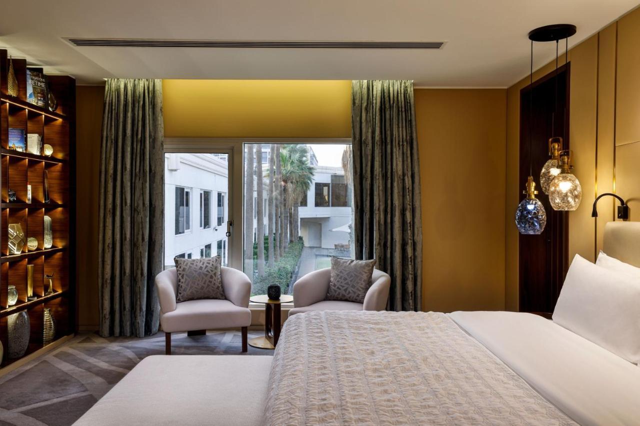 Le Meridien Dubai Hotel & Conference Centre Екстериор снимка The photo depicts a modern and elegantly designed hotel room. In the foreground, there is a large bed with a light-colored bedspread. On either side of the bed, there are stylish armchairs with decorative pillows. A small side table is positioned bet