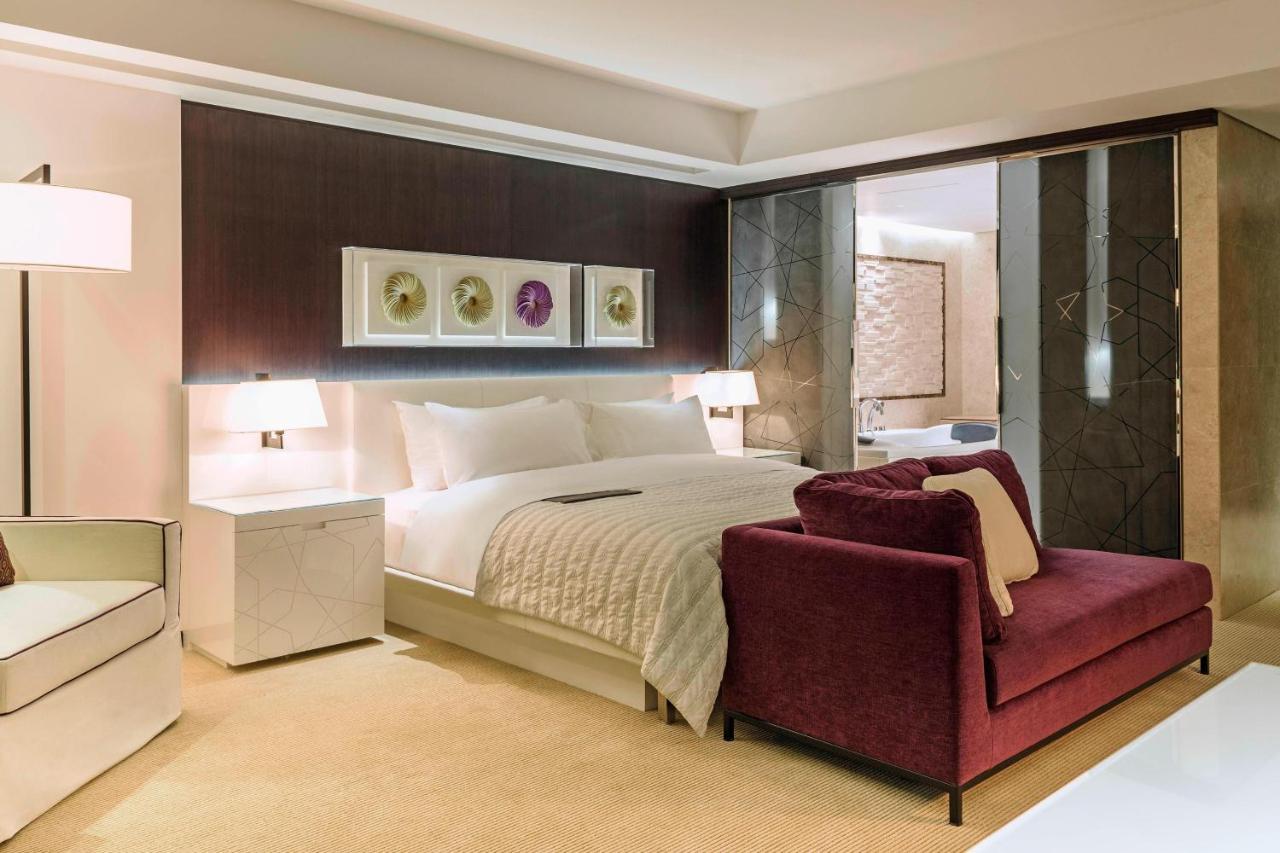 Le Meridien Dubai Hotel & Conference Centre Екстериор снимка The photo shows a modern hotel room featuring a spacious layout with a large bed, dressed in white linens, positioned against a dark accent wall. On either side of the bed are stylish bedside lamps. There is a burgundy armchair in front of the bed, p