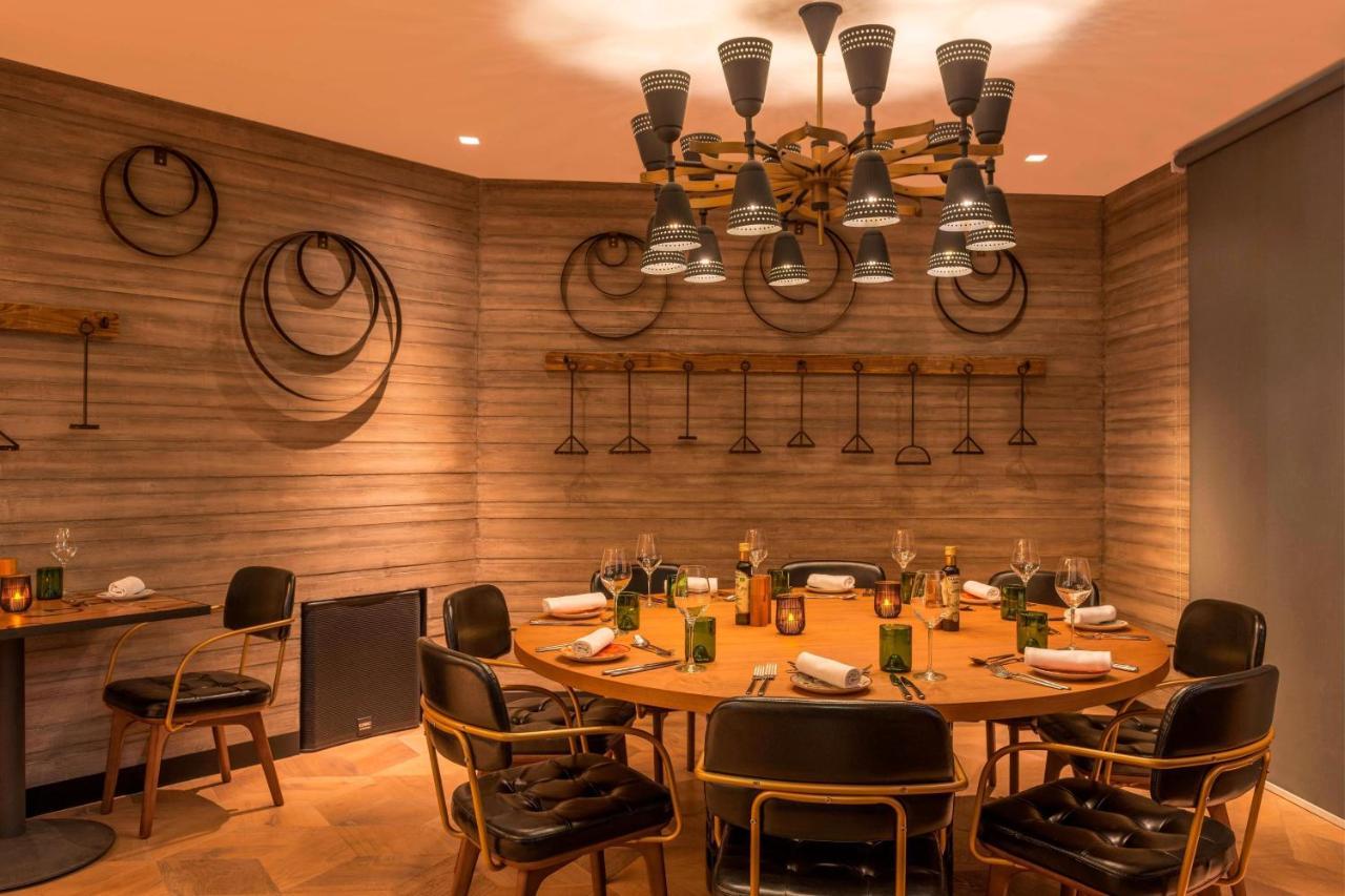Le Meridien Dubai Hotel & Conference Centre Екстериор снимка The photo shows a modern dining room with a circular wooden table surrounded by stylish black chairs. The walls are adorned with a textured design and feature some circular decorations, possibly made of metal or wood. Above the table, there is a uniq