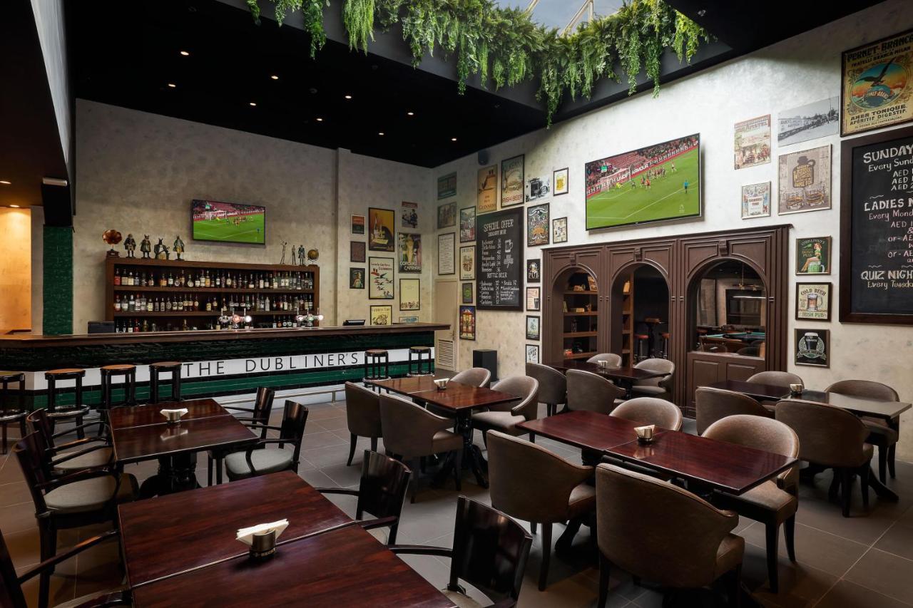 Le Meridien Dubai Hotel & Conference Centre Екстериор снимка The photo shows the interior of a restaurant or pub. The space features a bar area with a variety of bottles displayed on the shelves behind it. There are several tables arranged in the dining area, and the seating appears comfortable with upholstere