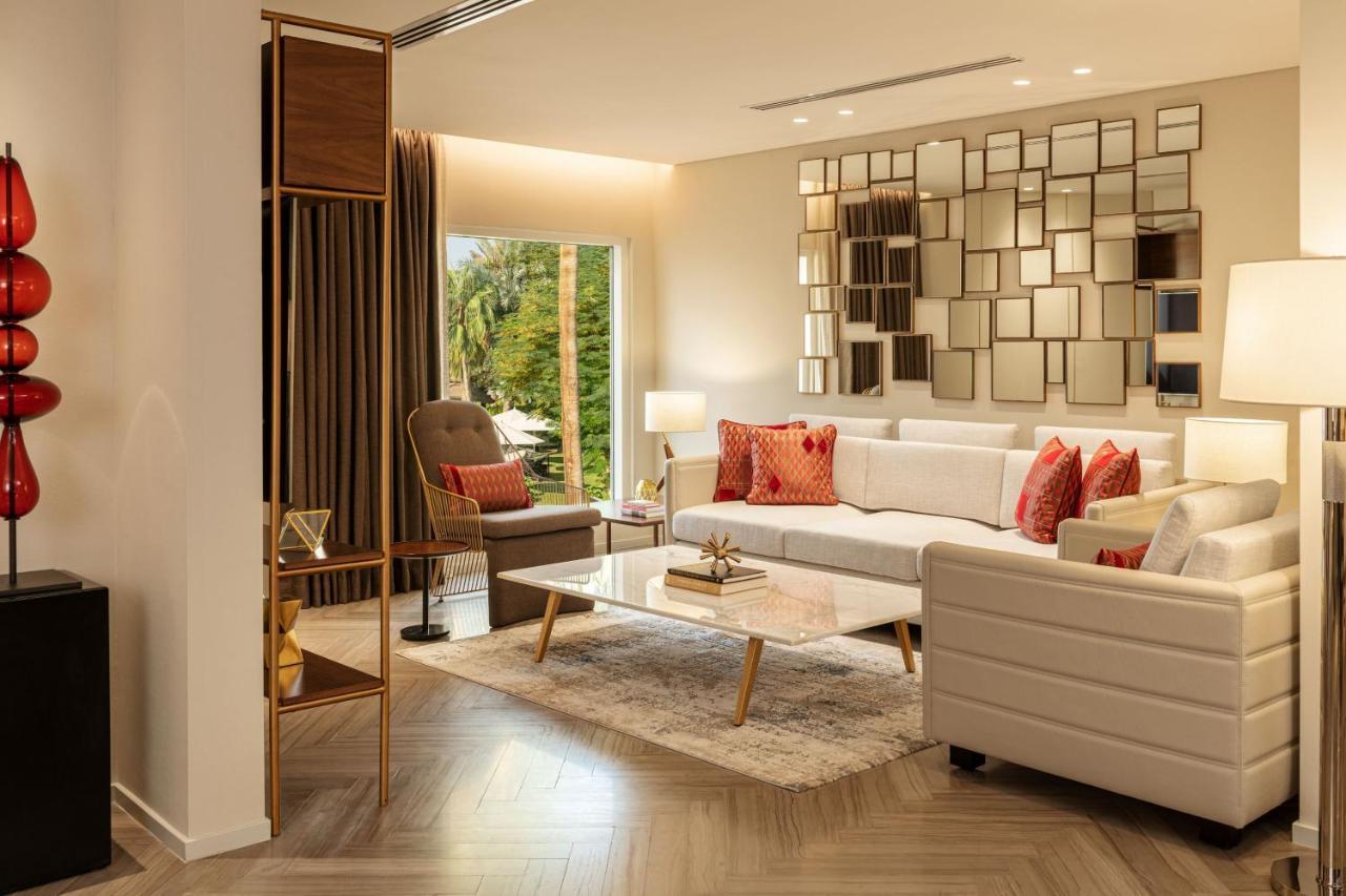 Le Meridien Dubai Hotel & Conference Centre Екстериор снимка The photo shows a modern living room interior. It features a white sofa adorned with red accent pillows, alongside a comfortable armchair in a muted color. A coffee table with a glass surface is positioned in front of the sofa, sitting on a light-col
