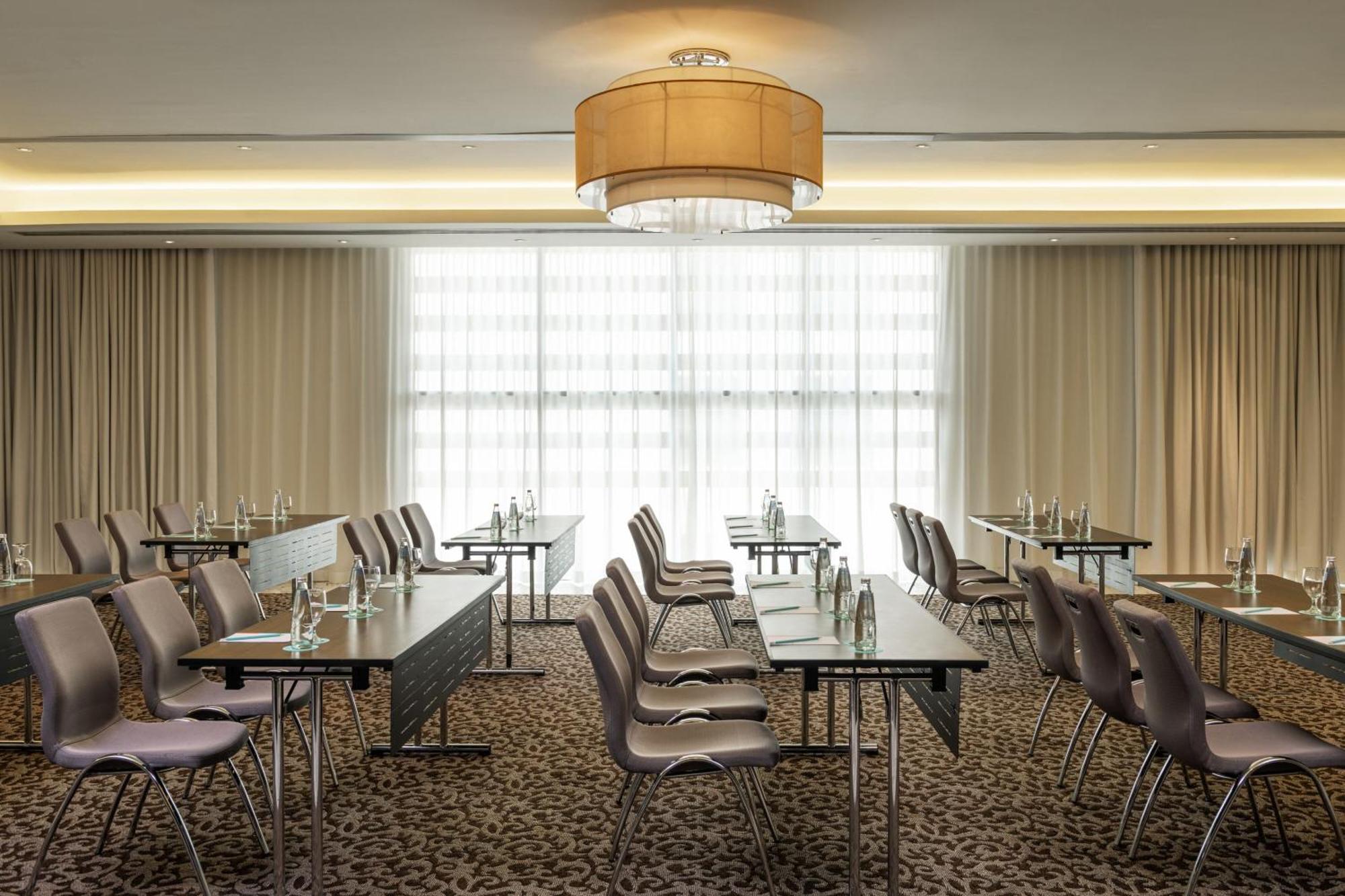 Le Meridien Dubai Hotel & Conference Centre Екстериор снимка The photo shows a conference room set up for meetings or presentations. There are several rows of tables with chairs arranged in a classroom style. Each table has a water bottle, suggesting that it is prepared for participants. The room is well-lit, 
